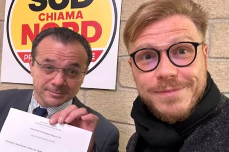 Two men posing for a selfie, one holding a paper.
