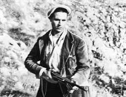 Black and white photo of a man holding a rifle outdoors.